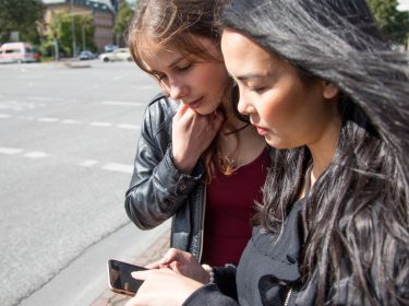Zwei junge Frauen an Straßenkreuzung schauen auf ein Smartphone