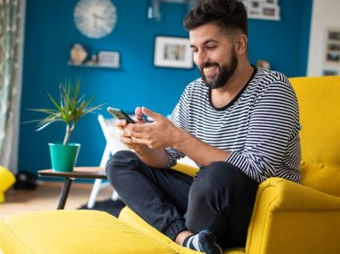 Mann schaut lächelnd auf sein Android-Smartphone.