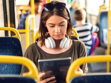 Frau sitzt mit 5G-Tablet im Bus.