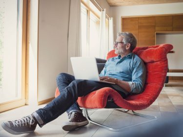 Mann sitzt in einem roten Stuhl mit seinem Laptop