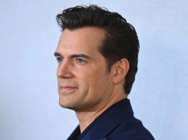 Auf diesem Bild zum Artikel „Voltron-Film mit Henry Cavill“ ist Henry Cavill in einem Profilporträt zu sehen. Er trägt ein dunkelblaues Sakko und blickt leicht lächelnd zur Seite. Sein Haar ist stilvoll nach hinten gekämmt, und der Hintergrund ist dezent und einfarbig, was den Fokus auf sein Gesicht lenkt. Cavill wirkt entspannt und selbstbewusst, passend zu seiner prominenten Rolle im Film.