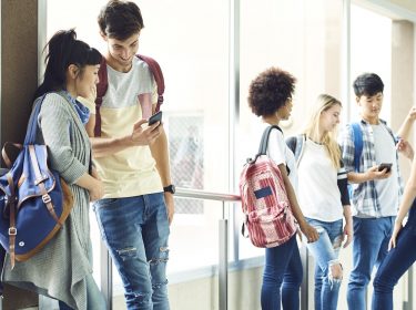 Schüler:innen stehen im Gang und schauen auf Handys