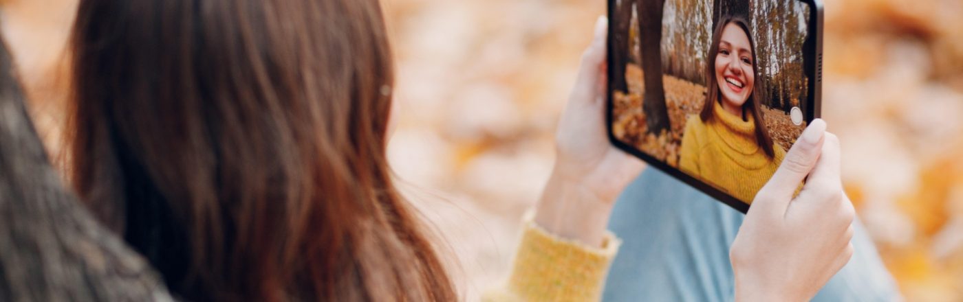 Junge Frau sitzt im Herbst im Park und macht Selfie mit dem iPad Pro 2021