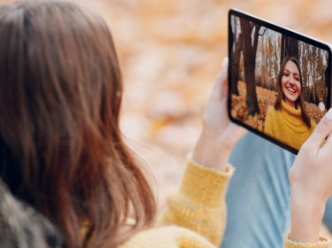Junge Frau sitzt im Herbst im Park und macht Selfie mit dem iPad Pro 2021