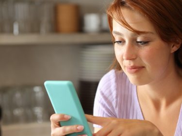 Rothaarige Frau in Küche spielt mit Smartphone