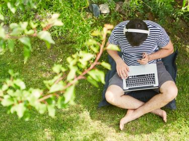 Ein Mann mit Kopfhörer und Laptop sitzt im Grünen.