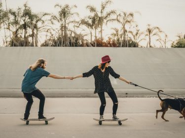 Zwei Personen stehen auf Skateboards und lassen sich von einem Hund ziehen