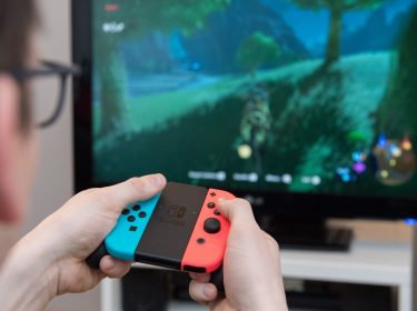 Mann vor Fernseher spielt Computerspielt mit Joy Cons der Nintendo Switch
