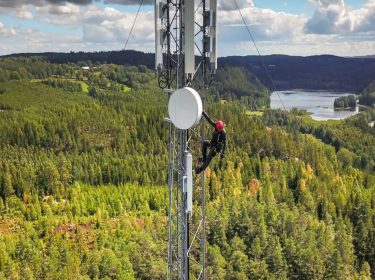 Ein Mensch klettern auf einem Sendemast innmitten eines Waldes.