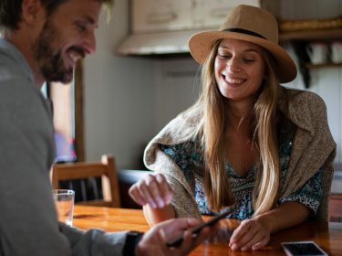 Lächelndes Paar sitzt am Küchentisch und schaut auf ein iPhone