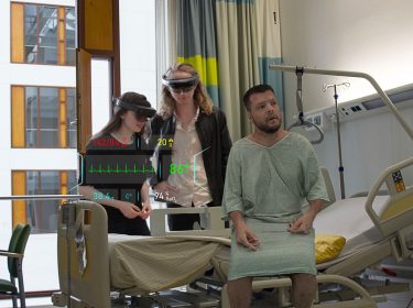 Ein Hologramm-Patient wird von zwei Medizin-Studierenden in einem Behandlungszimmer untersucht