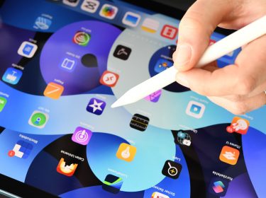 Hand mit Apple Pencil über einem iPad Air mit zahlreichen App-Symbolen