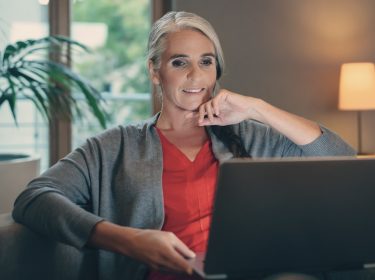 Frau schaut auf Laptop, der auf dem Schoss liegt.
