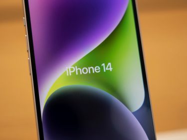 iPhone 14 in einem Apple Store vor orangefarbenem Hintegrund