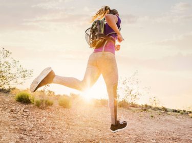 Sportliche Frau mit Rucksack läuft in Sonnenuntergang