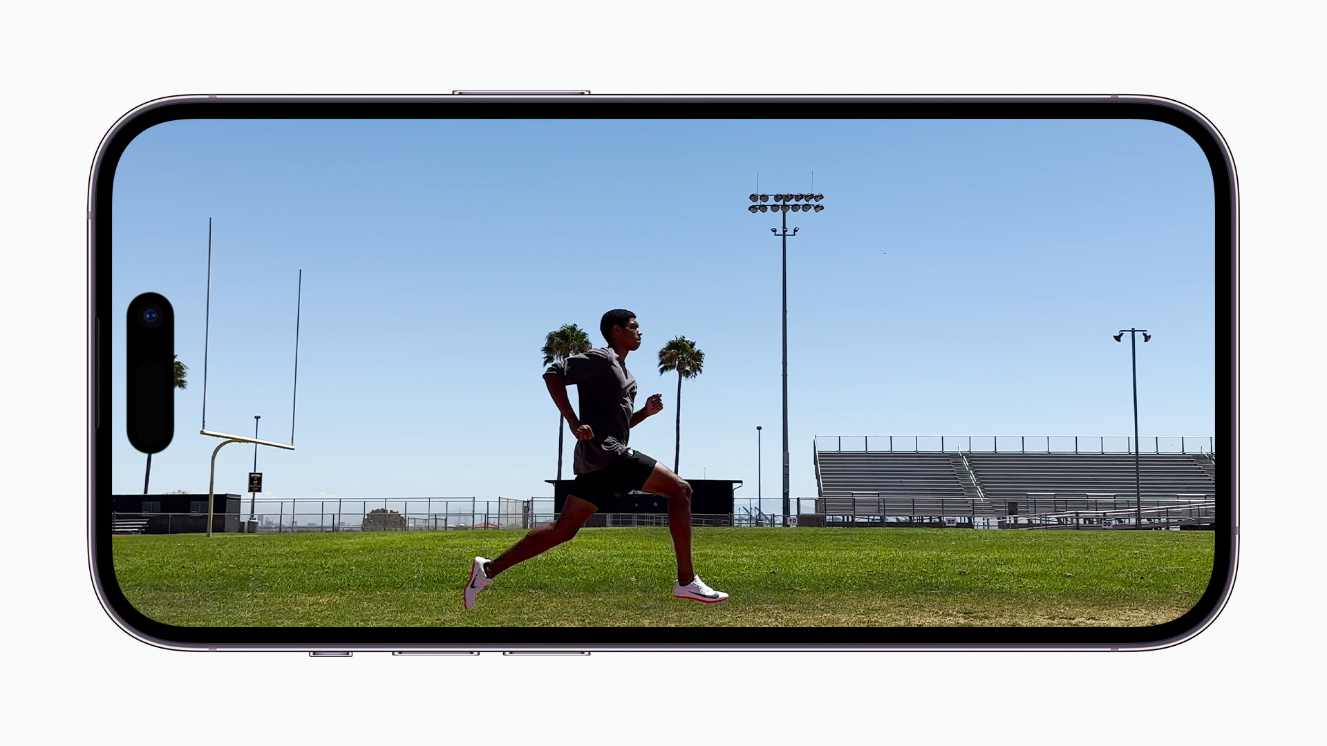 iPhone 14 Pro Max Display zeigt Läufer von der Seite auf einem Sportplatz mit Palmen