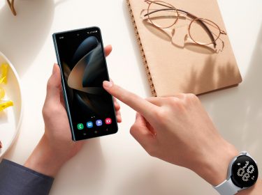 Linke Hand hält Galaxy Z Fold4 über Tisch, rechte Hand tippt auf Display