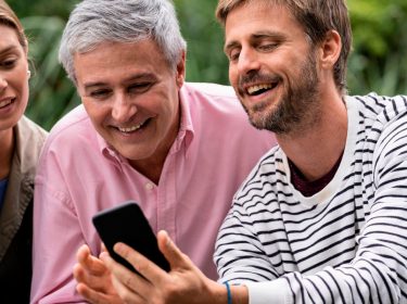 Junger Mann zeigt einem älteren Herren und einer jungen Frau etwas auf seinem Smartphone