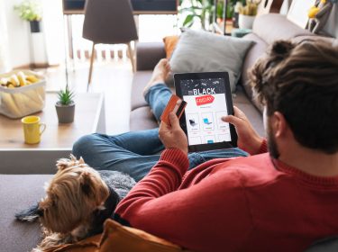 Mann liegt auf der Couch und schaut nach Angeboten am Black Friday
