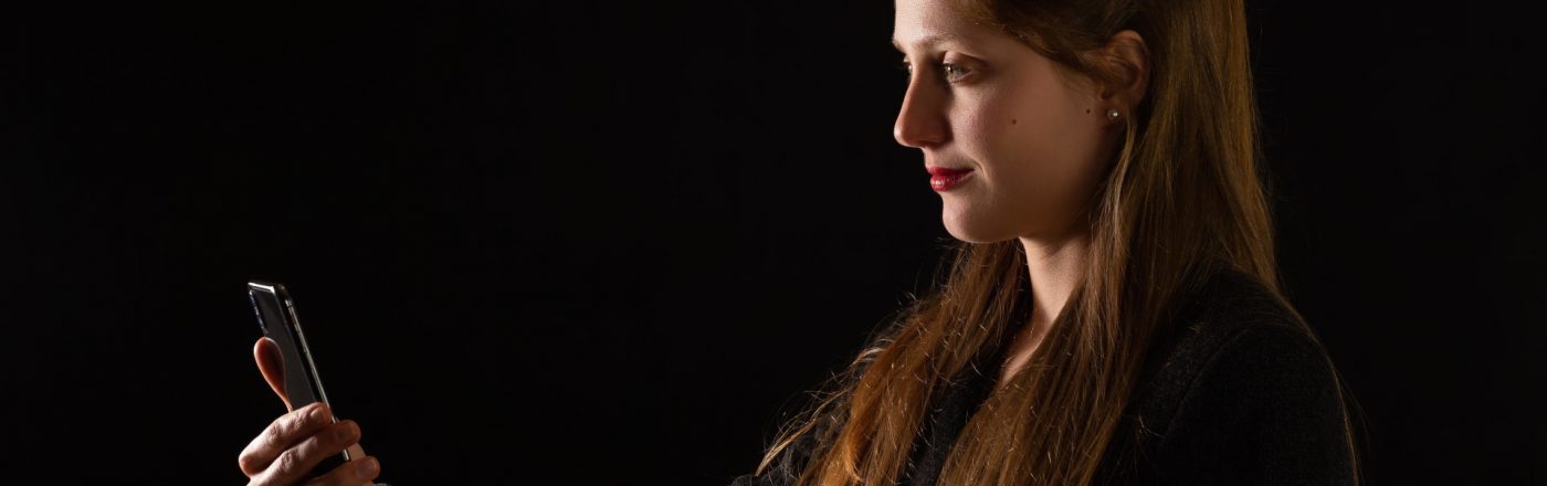 Junge Frau im Profil mit langen Haaren guckt auf ihr iPhone zur Gesichtsentsperrung