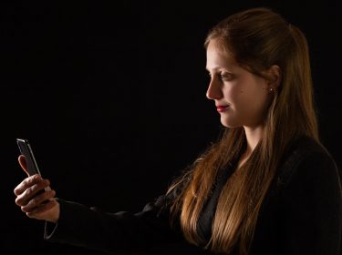 Junge Frau im Profil mit langen Haaren guckt auf ihr iPhone zur Gesichtsentsperrung