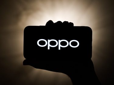 Silhoutte einer Hand hält Smartphone mit OPPO-Logo vor dunklem Hintergrund mit Lichtquelle