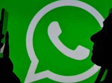 Silhouette einer Frau mit Smartphone vor dem WhatsApp-Logo