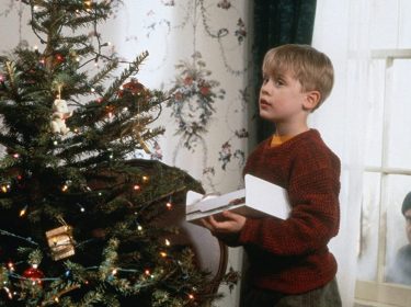 Kevin steht mit Tannenbaumschmuck vor dem Weihnachtsbaum.