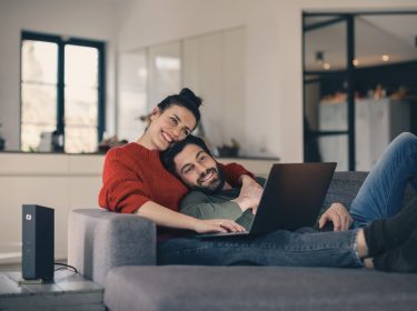 Ein Paar sitzt gemütlich auf der Couch mit einem Laptop auf dem Schoß
