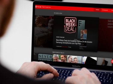 Mann sitzt vor MacBook Pro und hat die Finger auf der Tastatur, im Display ist die featured-Homepage zu sehen.