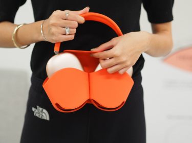 Junge Frau packt ihre AirPods Max in eine passende Hülle in elegantem Orange.