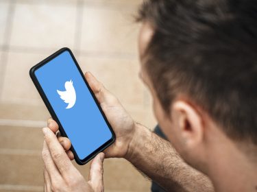 Twitter-Logo auf einem Smartphone, gehalten von einem jungen Mann