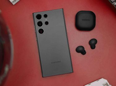 Das Samsung Galaxy S23 Ultra liegt mit der Vorderseite auf einer roten Fläche neben Samsung-Kopfhörern