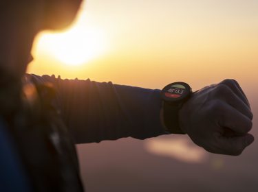 Ein junger Herr blickt auf seine Smartwatch, bei Sonnenuntergang.