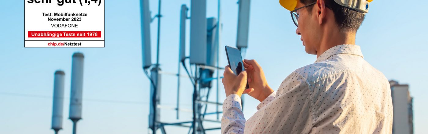 Ein Mann steht mit einem Smartphone und einem Bauarbeiterhelm vor einem Funkmast und prüft seine Verbindung. Ein Chip-Testsiegel ist im linken Bildbereich zu sehen mit der Gesamtnote 