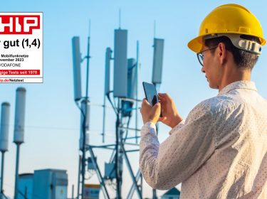Ein Mann steht mit einem Smartphone und einem Bauarbeiterhelm vor einem Funkmast und prüft seine Verbindung. Ein Chip-Testsiegel ist im linken Bildbereich zu sehen mit der Gesamtnote 