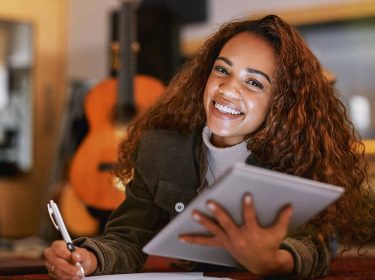 Eine Frau hält ein iPad in der Hand und macht sich Notizen auf einem Block