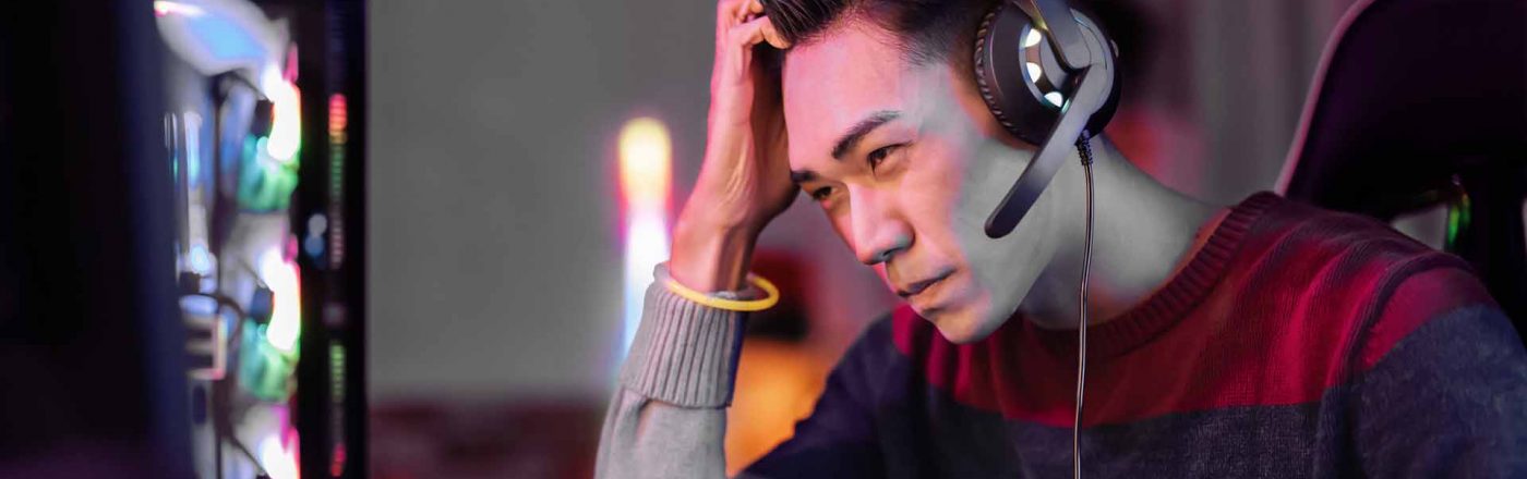 Ein Gamer sitzt am Schreibtisch und fasst sich an den Kopf