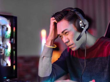 Ein Gamer sitzt am Schreibtisch und fasst sich an den Kopf