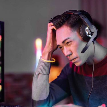 Ein Gamer sitzt am Schreibtisch und fasst sich an den Kopf
