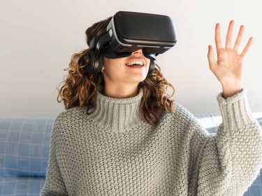 Eine Frau trägt eine VR-Brille und sitzt auf einem Sofa