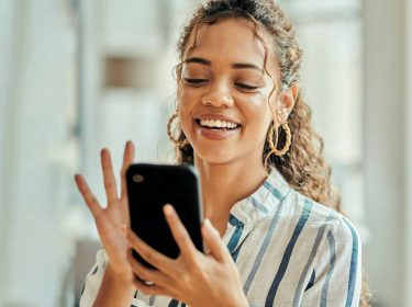 Eine Frau hält ein Handy in der Hand und lächelt.