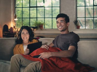 Mann und Frau sitzen gemeinsam auf dem Sofa und schauen Fernsehen