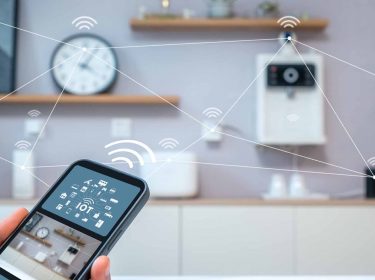 Ein Smartphone in der Hand steuert Geräte im Smart Home an