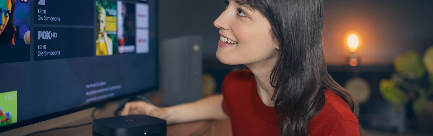 Bei der Auswahl der Vodafone Premium Plus Sender blickt eine junge Frau lächelnd auf den Fernseher, während sie eine Fernbedienung in der Hand hält.