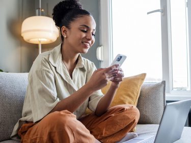 Frau sitzt auf dem Sofa und unternimmt Einstellungen zur Datensicherung an ihrem Smartphone