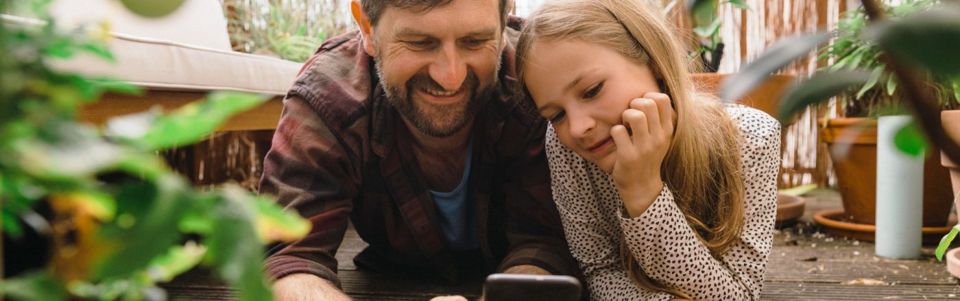 Vater und Tochter mit Smartphone auf dem Balkon