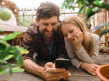 Vater und Tochter mit Smartphone auf dem Balkon