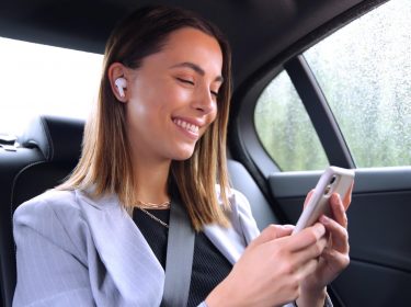 Junge Frau im Auto mit Smartphone und In-Ears