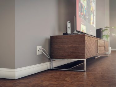 In einer sonnendurchfluteten Wohnung steht ein Fernseher auf einer eleganten Holzkommode. Im Fokus steht der Kabelanschluss des Fernsehers.